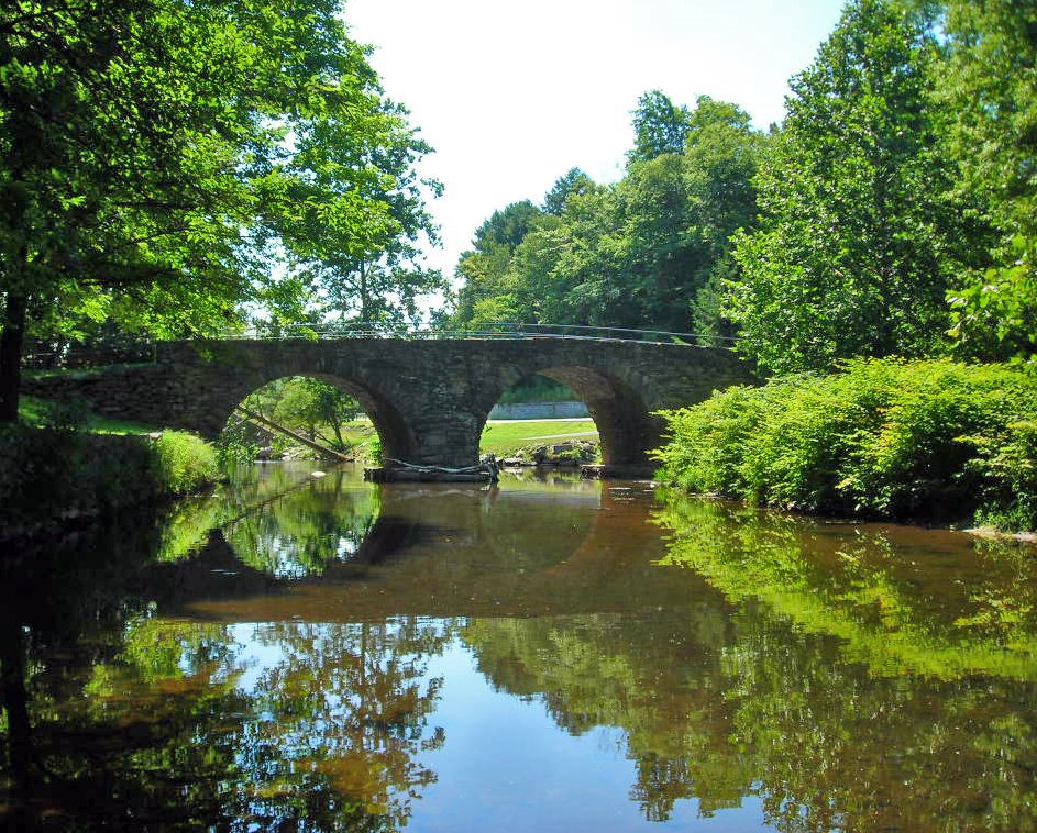 A stone arch and its reflection in water.